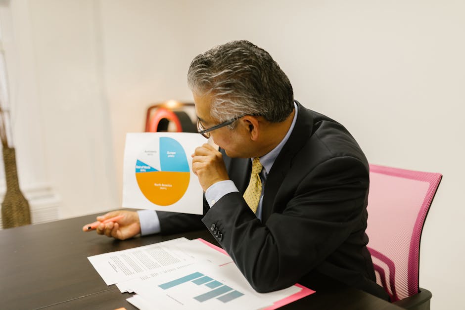 A businessman in a suit reviews pie chart documents at his office desk.